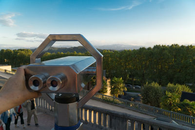 Cropped hand of person holding coin-operated binoculars against sky