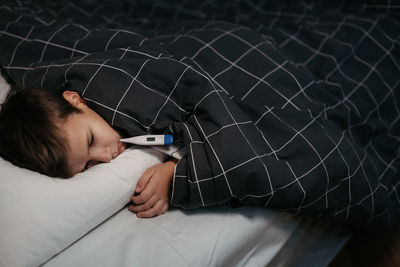 Sad child laying in bed with thermometer in his mouth. temperature measurement. 