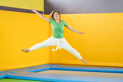 Full length of woman jumping against yellow wall