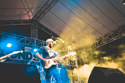 Man playing guitar while standing on illuminated stage at night