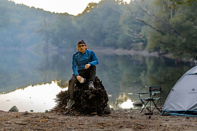 Man sitting by lake against mountain