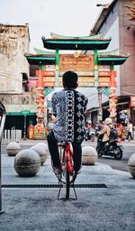 Rear view of man sitting on street against building