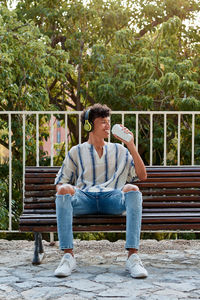 Young boy with afro hair drinks coffee while he is sitting on a bench