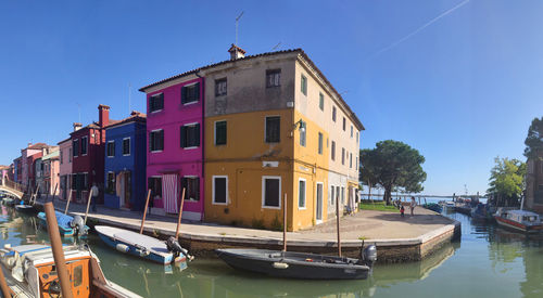 Boats moored on canal amidst buildings in city against sky