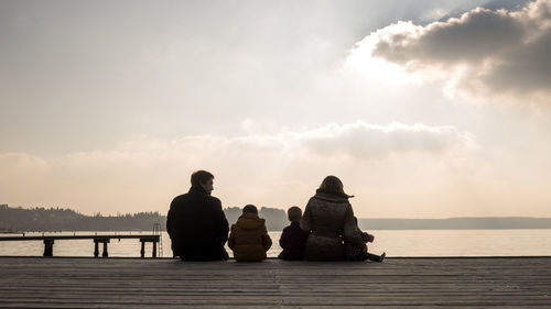 Rear view of parents with children sitting on pier over lake at sunset