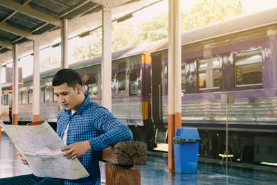 Man reading map while sitting at railroad station platform