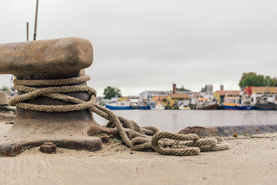 Close-up of rope tied to moored at harbor against sky