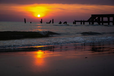 Silhouette people on beach against orange sky