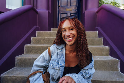 Happy young woman with curly hair sitting on staircase