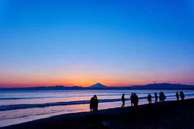 Silhouette people on beach against sky during sunset