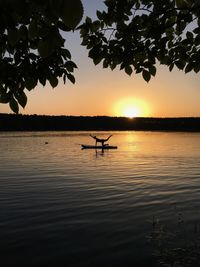 Silhouette women doing yoga over raft on lake against sky during sunset