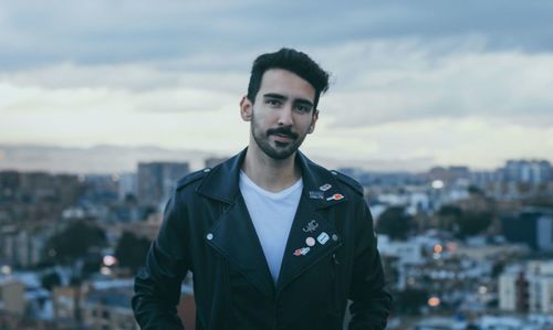 Portrait of young man standing against sky in city