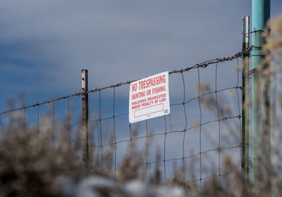 Low angle view of no trespassing sign on fence against sky