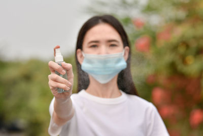 Portrait of young woman wearing mask holding hand sanitizer outdoors