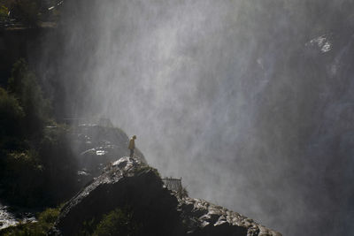 Full length of man standing on rock against waterfall