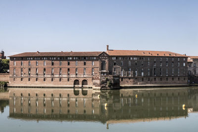 Reflection of building in river against clear sky