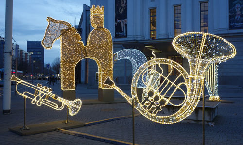 Illuminated ferris wheel against building at night