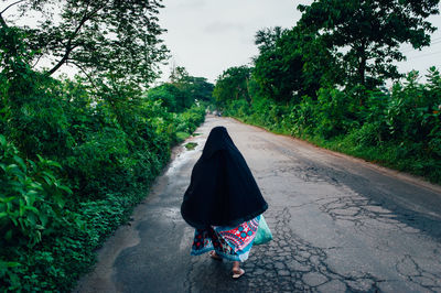 Rear view of woman walking on road amidst trees