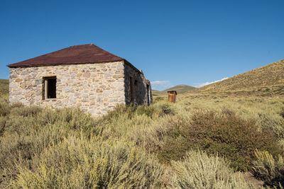 Abandoned stone building/cabin/house with wooden outhouse toilet, bodie, california ghost town