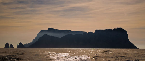 Silhouette rock formations by sea against sky during sunset