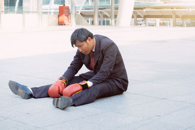Side view of young woman sitting on footpath in city