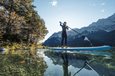 Germany, bavaria, garmisch partenkirchen, young woman stand up paddling on lake eibsee