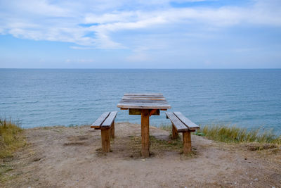 Chair on table by sea against sky