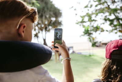 Teenage boy photographing through smart phone by sister during vacation