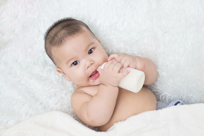 Portrait of cute boy with milk bottle lying on bed