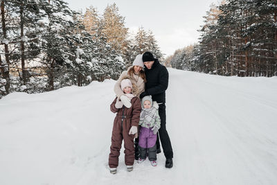 Dad and mom and two daughters walk through the snowy forest