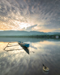 Boat moored in lake against sky during sunset