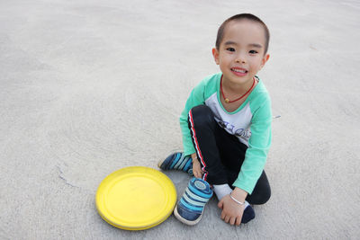 Portrait of boy sitting with plastic disc on footpath at park