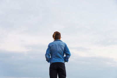 Rear view of woman standing against cloudy sky