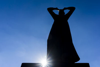 Low angle view of silhouette man standing against blue sky