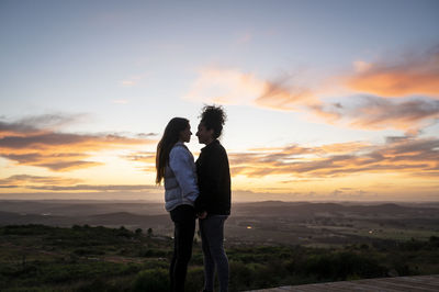 Lesbian couple holding hands and standing close to each other outdoors.