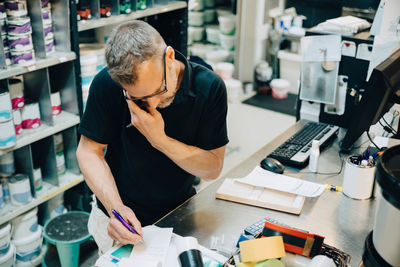 High angle view of salesman writing while talking on phone in store