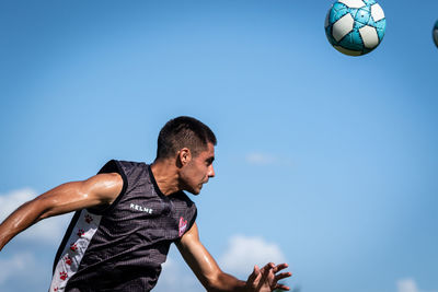 Low angle view of man playing soccer ball against blue sky