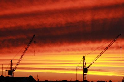 Silhouette cranes against sky during sunset