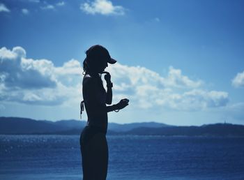 Side view of woman standing by sea against sky