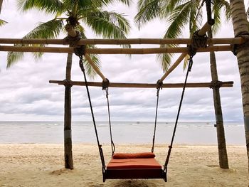 Empty swing hanging at beach against sky