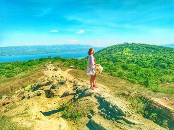 Side view of young woman standing on mountain against sky during sunny day