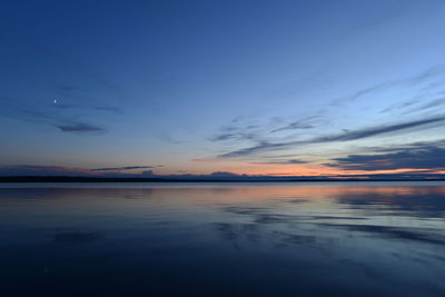 Moonrise in twilight light in the blue sky at sunset over the quiet mirror water of the lake