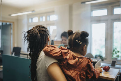 Mother carrying daughter while standing at reception desk in hospital