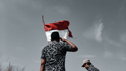 Low angle view of man holding man standing against sky