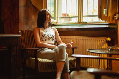 Smiling young woman sitting on chair by window