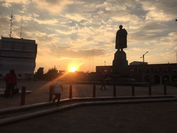 Statue in city at sunset