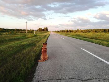 Road passing through field against sky