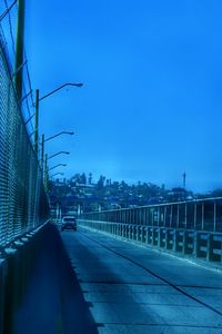 Road leading towards city against clear blue sky