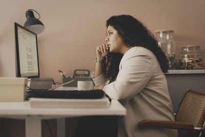 Side view of thoughtful businesswoman looking at computer while sitting at desk in office