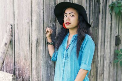 Young woman looking away while standing by wooden wall